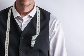 Well dressed tailor in white shirt and black suit vest have measuring tape hanging around neck....