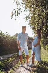 Expecting man and woman walk along the path across the field with sunflowers in beautiful summer evening