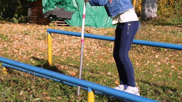 Girl like equilibrist walking on narrow crossbar with long pole in autumn park