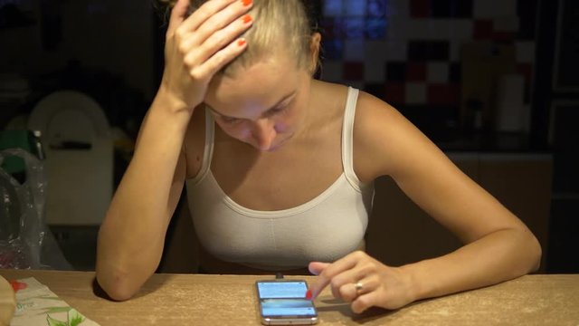 Portrait of sad woman scrolling the smartphone while sitting in the kitchen
