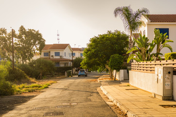 Countryside street with cottages, homes, palm trees and car at sunset