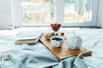 appetizing breakfast and open book on bed in bedroom