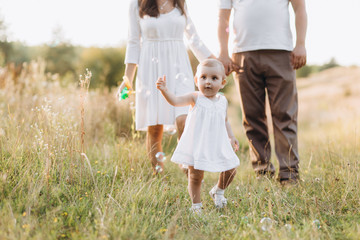 Fototapeta premium Young parents walk with their lovely little daughter in jeans dress across the field