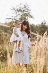 Beautiful portrait of charming mother and lovely little daughter walking across the field in the rays of evening sun