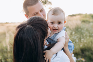 Fototapeta premium Warm hugs of young parents and their little daughter standing in the summer field