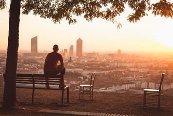 Man on a bench relaxing and enjoying the summer sunrise over a city. Lyon, France.