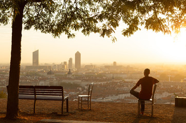 Man on a bench relaxing and enjoying the summer sunrise over a city. Lyon, France.