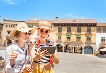 vacation and travel concept - two beautiful girls toursits looking into tablet pc in the old city...