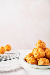 Bunch of fresh cream puff cakes on a white plate and wire rack on white marble table over pink background with copy space. Selective focus.