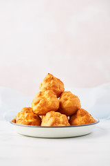 Bunch of fresh cream puff cakes on a white plate on white marble table over pink background with copy space. Selective focus.