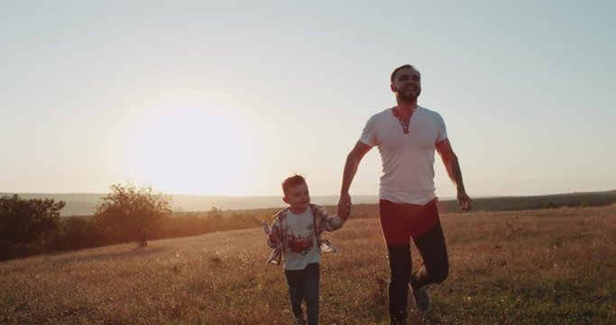 Dad with his son running at nature , looking some fare away, background amazing sunset.