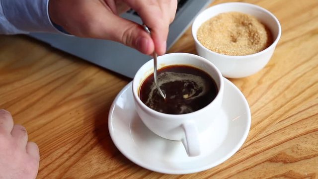 Close-up of man's hand pours sugar into a cup of coffee at the bar, and stir it