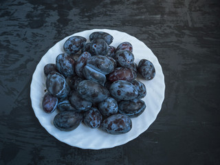 white plate with ripe prunes on a dark wooden background