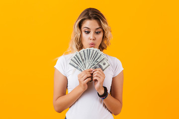 Photo of european woman in basic clothing holding fan of dollar money, isolated over yellow background