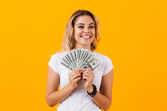 Photo of caucasian woman in basic clothing holding fan of dollar money, isolated over yellow background