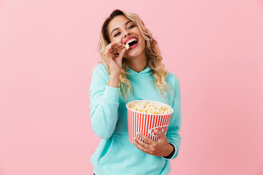 Image of beautiful european woman 20s eating popcorn from bucket, isolated over pink background