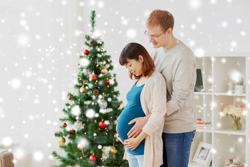 pregnancy, winter holidays and people concept - happy pregnant wife with husband at home at christmas