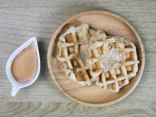 Waffles and honey in a cup placed on a wooden floor.