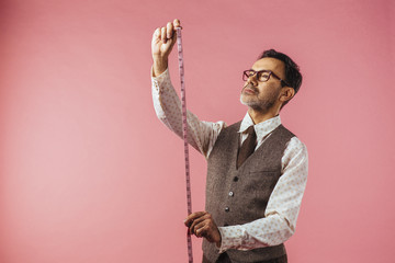 Horizontal portrait of a tailor holding fabric measure, isolated on pink studio background