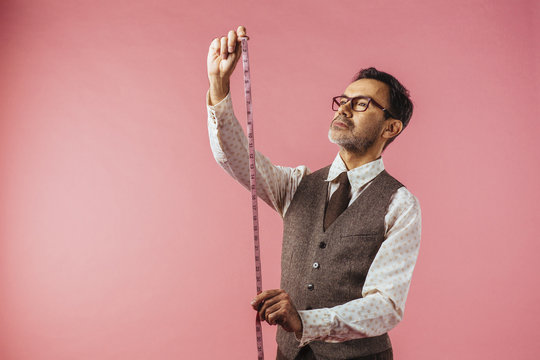 Horizontal portrait of a tailor holding fabric measure, isolated on pink studio background