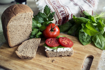 Sandwich with ricotta cheese, tomato and spinach on a cutting board.