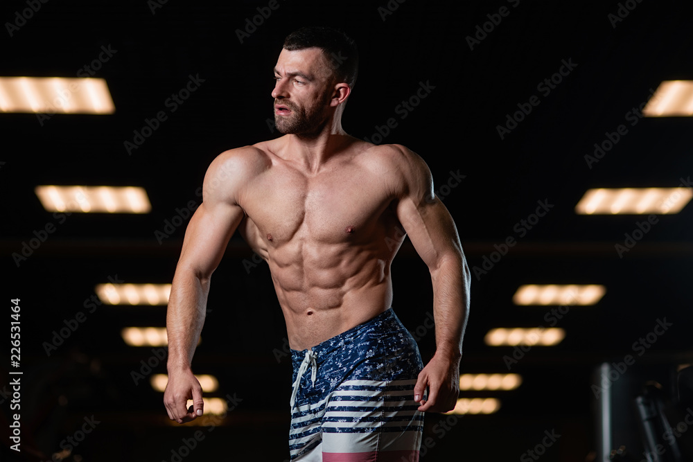 Wall mural athletic man with a muscular body poses in the gym, showing off his muscles. the concept of a health