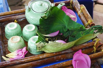 Celadon glazed tea set with pink flower petals and lotus tea wrapped in a lotus leaf on a bamboo...