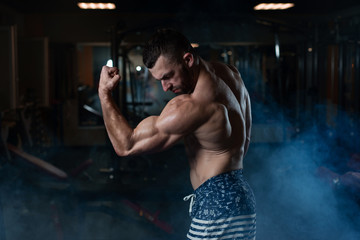 Athletic man with a muscular body poses in the gym, showing off his biceps and back. The concept of a healthy lifestyle