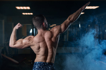 Athletic man with a muscular body poses in the gym, showing off his biceps and back. The concept of a healthy lifestyle