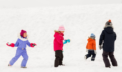 Fototapeta na wymiar childhood, leisure and season concept - group of happy little kids in winter clothes playing outdoors