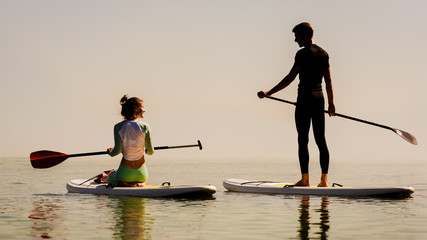 Silhouette of two young people on a paddle board