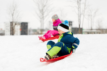 childhood, sledging and season concept - happy little kids sliding on sleds down snow hill in winter