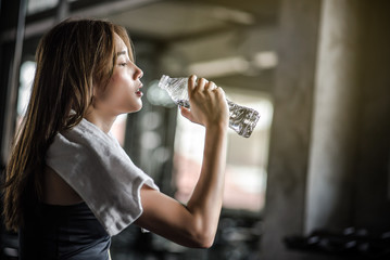 Young athletic fitness woman drinking water from bottle  in gym.