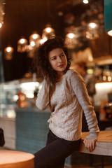 beautiful brunette in a gray knitted sweater posing on camera in a cozy warm cafe in a cold autumn