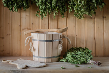 A wooden bucket and a birch broom in a Russian bath. Sauna. Free space on a wooden background.