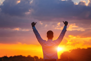 happy businessman, standing in field over wind background with his hands up and thumbs up