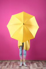 Woman hiding behind yellow umbrella near color wall