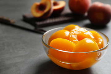 Glass bowl with conserved peach halves on grey table. Space for text