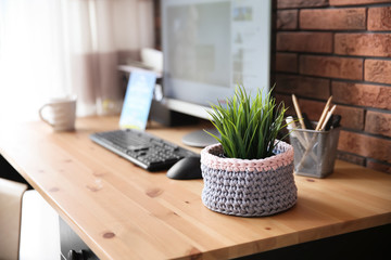 Knitted flowerpot cover with plant on office table, space for text. Interior element