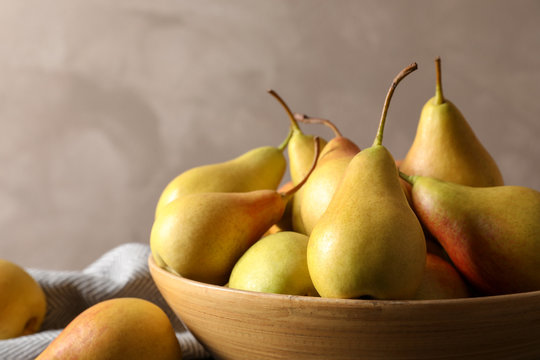 Bowl with ripe pears on table against grey background