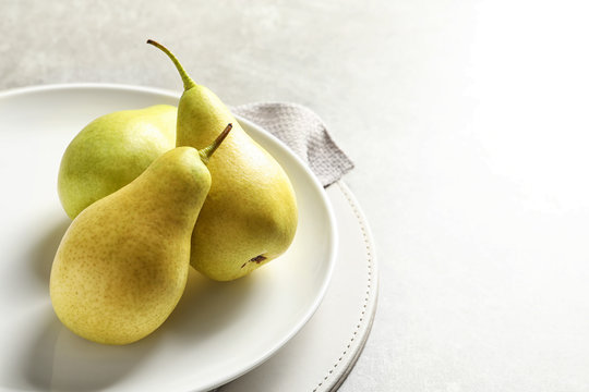 Plate with ripe pears on light background. Space for text