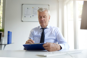 Thinking senior businessman writing something