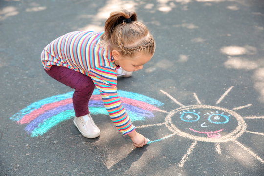 Little child drawing with colorful chalk on asphalt