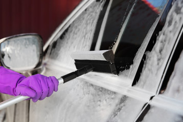 Worker cleaning automobile with squeegee at car wash, closeup