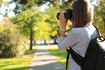 Young female photographer taking photo with professional camera in park. Space for text
