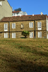 Old house with stone bricks, roof tiles, white windows and palm tree from a public park. Sunset, Santiago de Compostela, Spain.