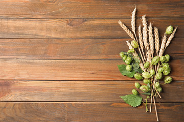 Fresh green hops and wheat spikes on wooden background, top view with space for text. Beer...