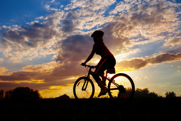 Fototapeta na wymiar Silhouette of girl cyclist riding against the sunset