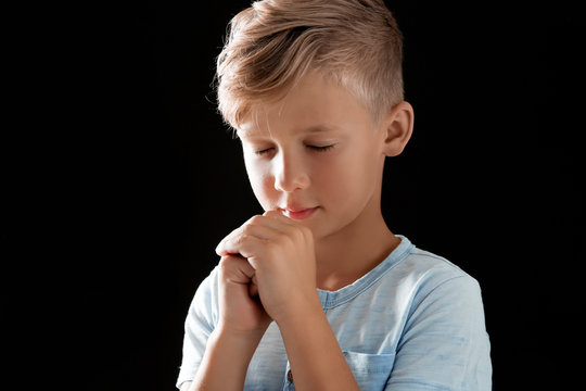 Little boy with hands clasped together for prayer on black background