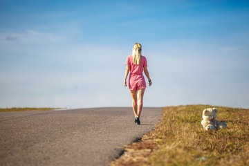 girl in plaid suit leaves on asphalt road from teddy bear. concept of ending childhood